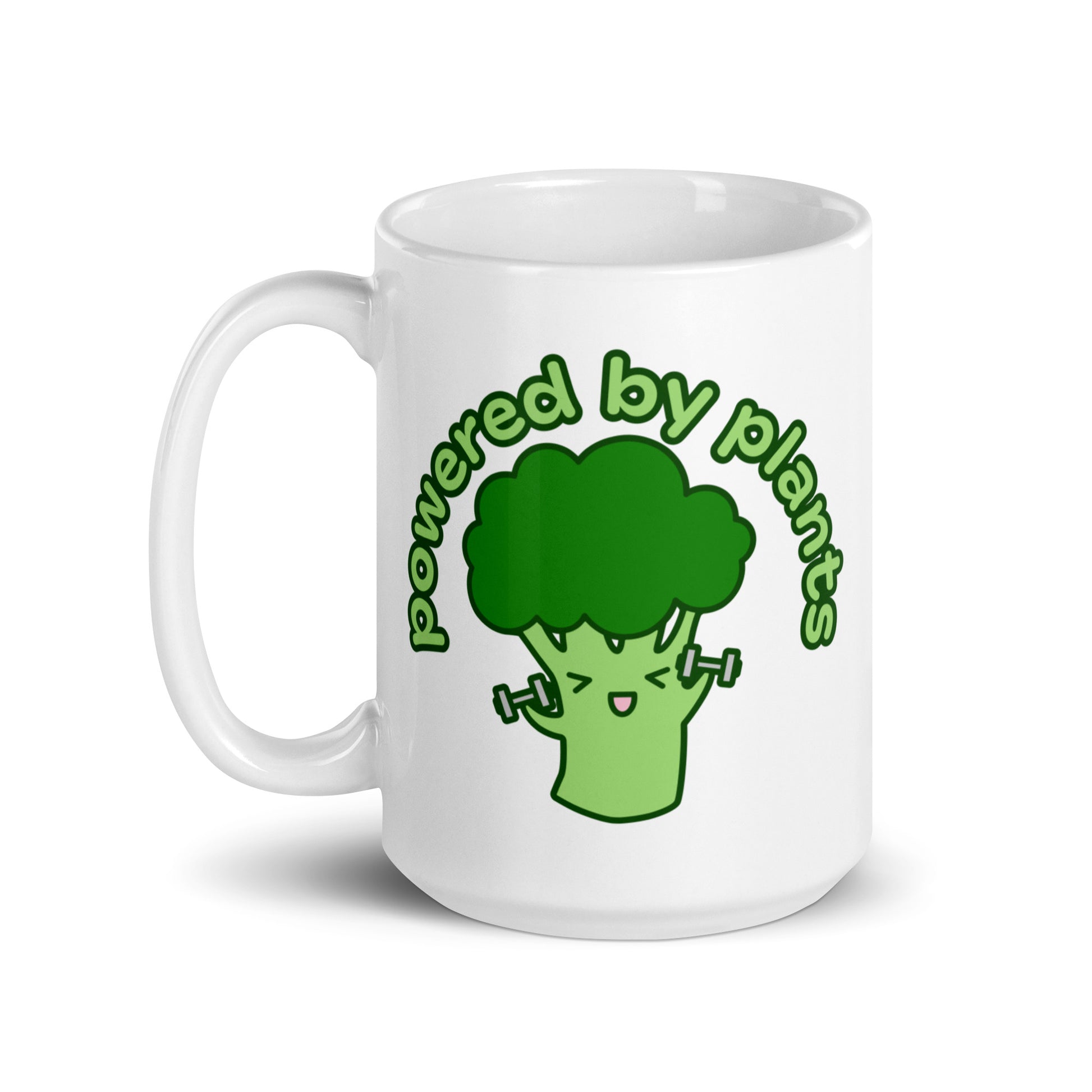 A white 15 ounce ceramic coffee mug featuring a cute illustration of a cartoon broccoli. The broccoli is excitedly lifting weights and text above him in an arc reads "powered by plants".
