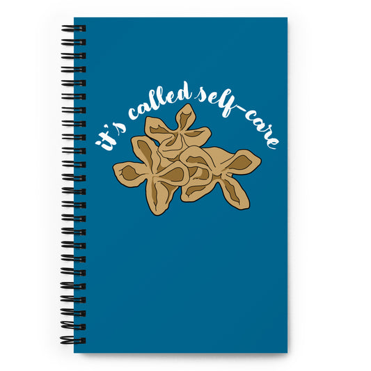A blue o-ring bound notebook featuring an illustration of three pieces of crab rangoon on the cover. Text above the crab rangoon reads "it's called self-care" in a cursive script.