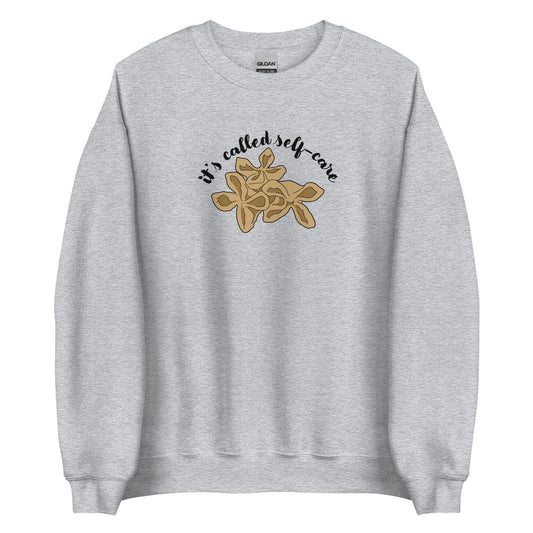 A gray crewneck sweatshirt featuring an illustration of three pieces of crab rangoon. Text in an arc above the crab rangoon reads "it's called self-care" in a cursive script.