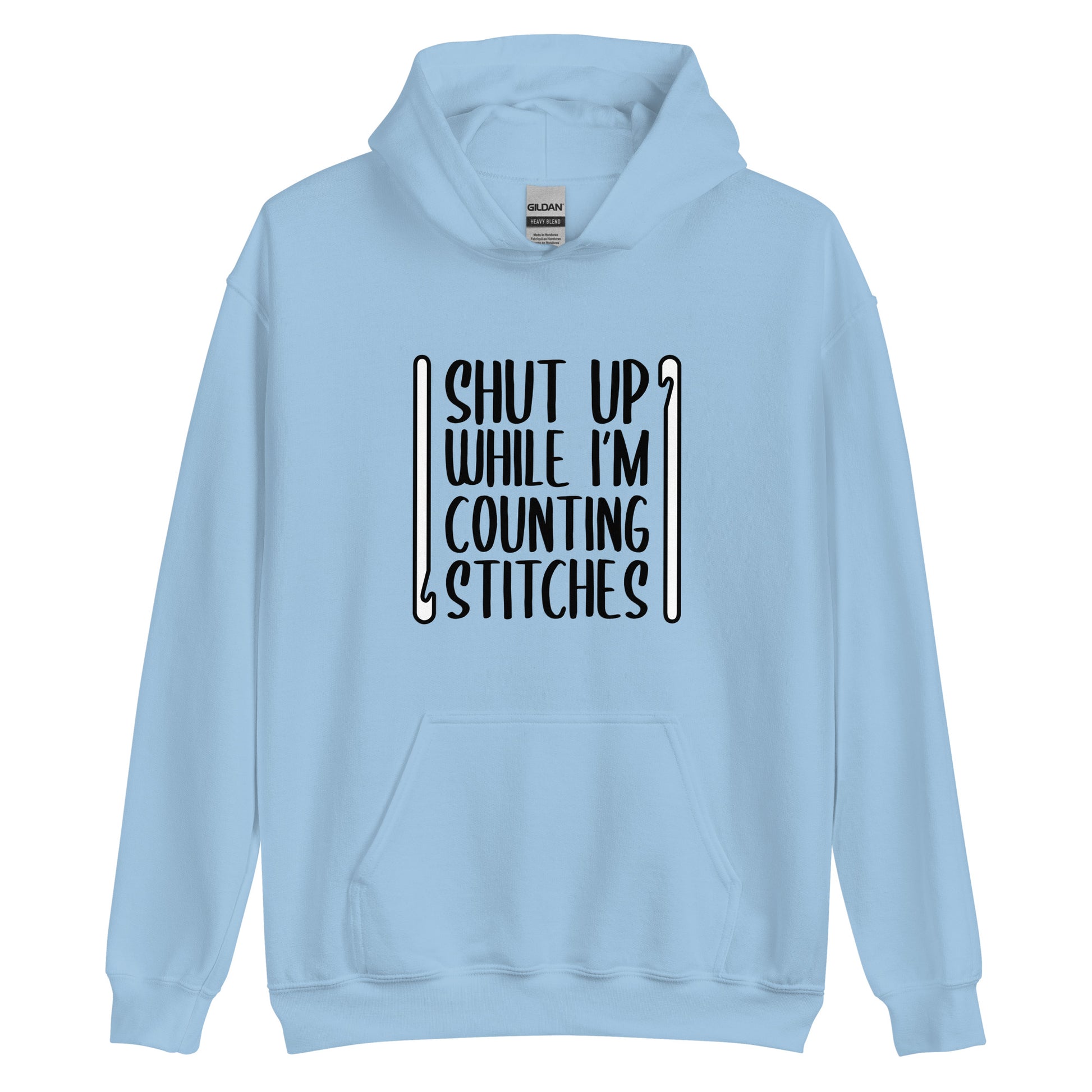A light blue hooded sweatshirt featuring black text that reads "Shut up while I'm counting stitches." The text is framed by a crochet hook to the left and right.