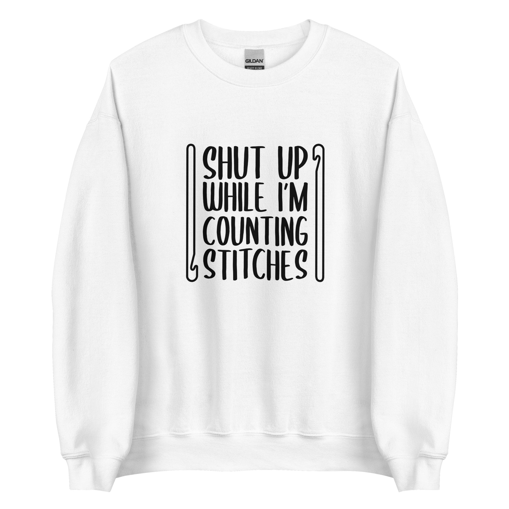 A white crewneck sweatshirt featuring black text that reads "Shut up while I'm counting stitches." The text is framed by a crochet hook to the left and right.