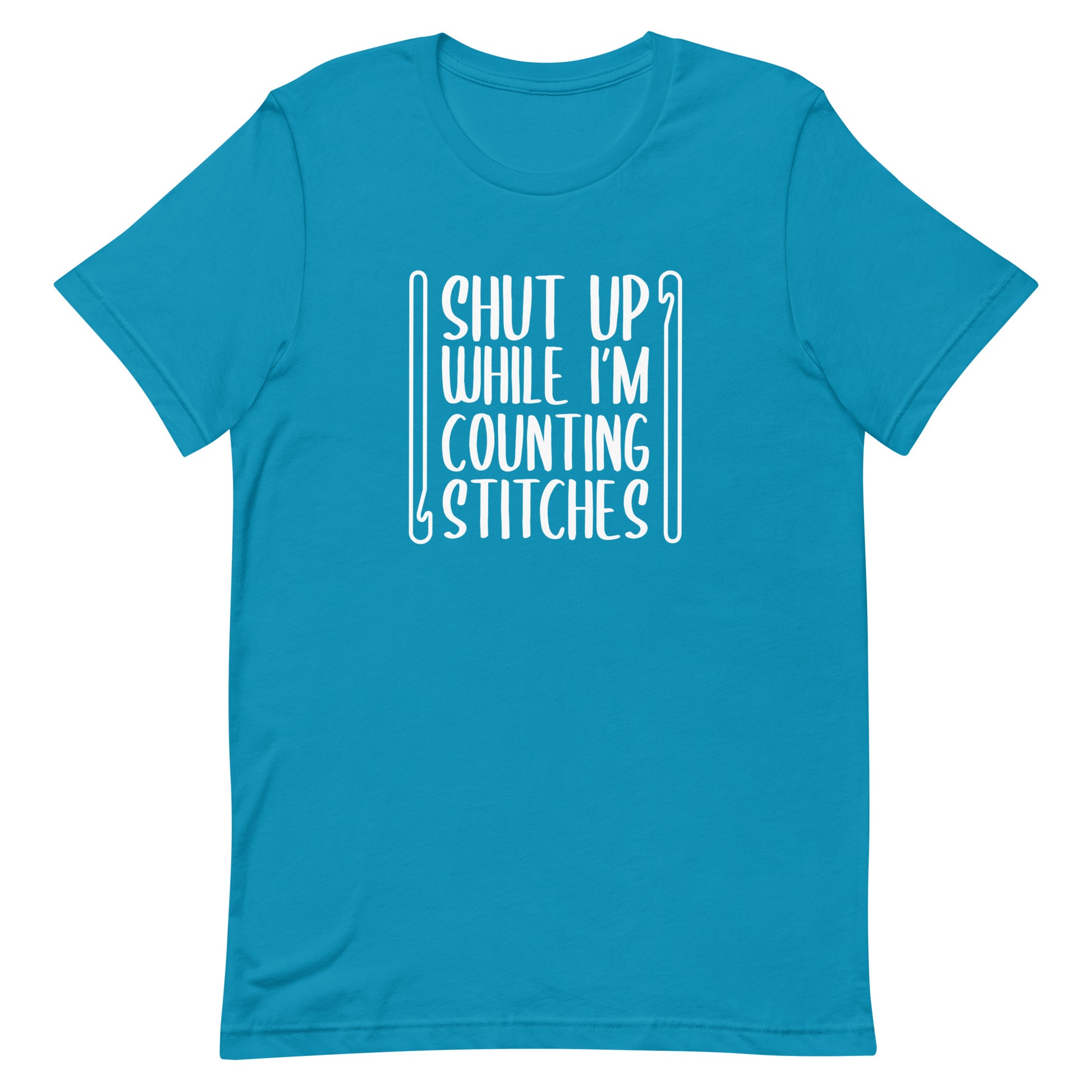 A blue crewneck t-shirt featuring white text that reads "Shut up while I'm counting stitches." The text is framed by a crochet hook to the left and right.