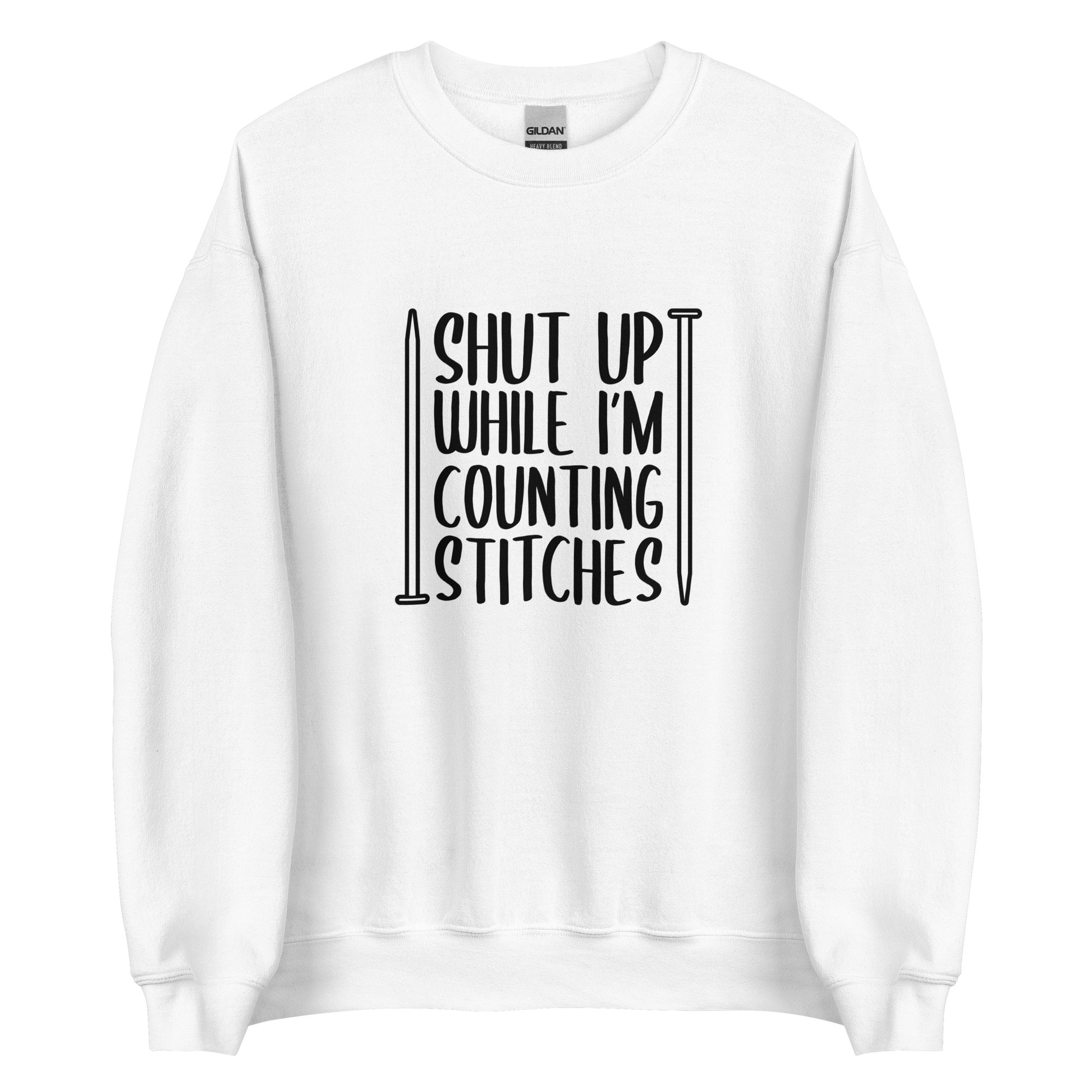 A white crewneck sweatshirt with black text surrounded by two knitting needles. The text reads "Shut up while I'm counting stiches".