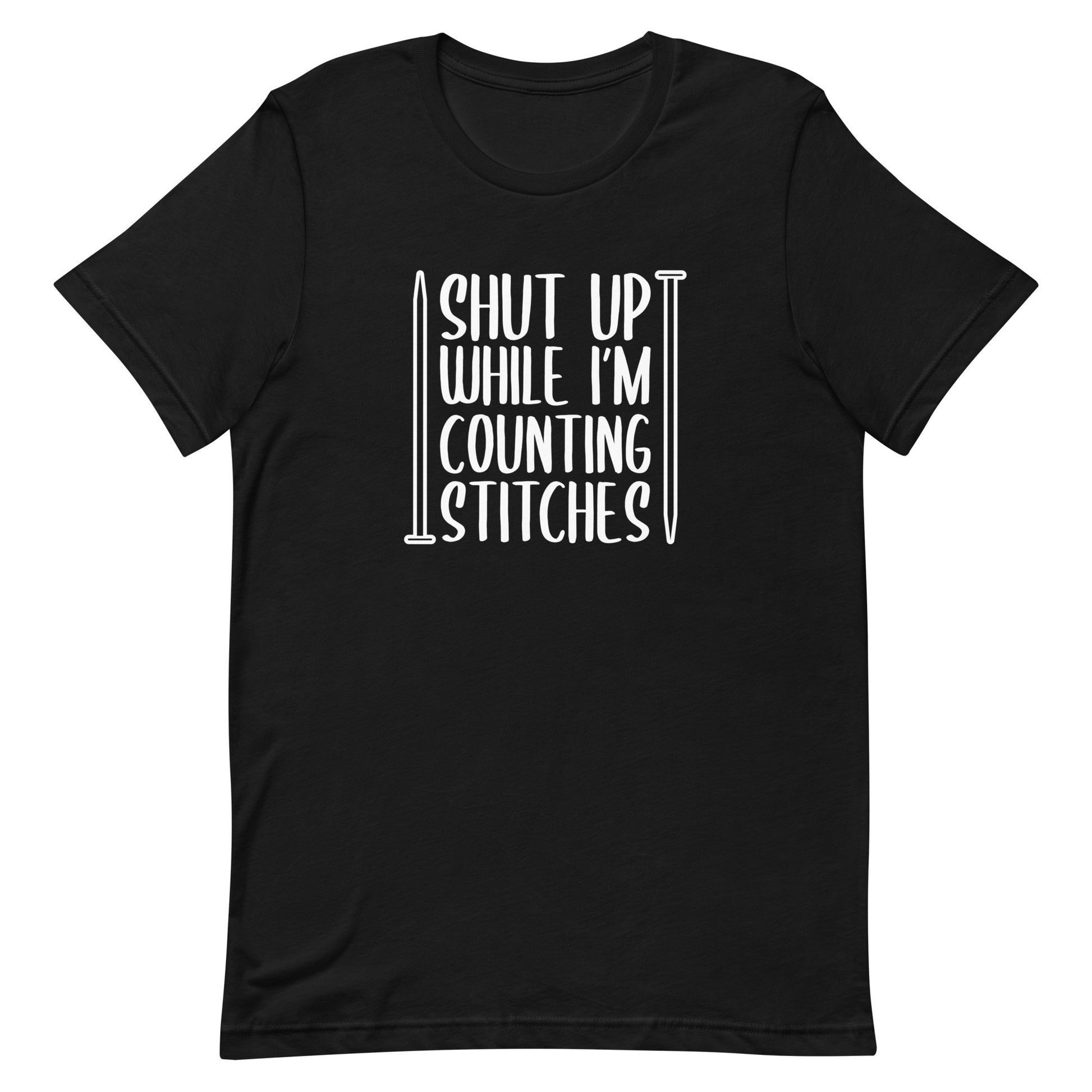 A black crewneck t-shirt with white text surrounded by two knitting needles. The text reads "Shut up while I'm counting stiches".
