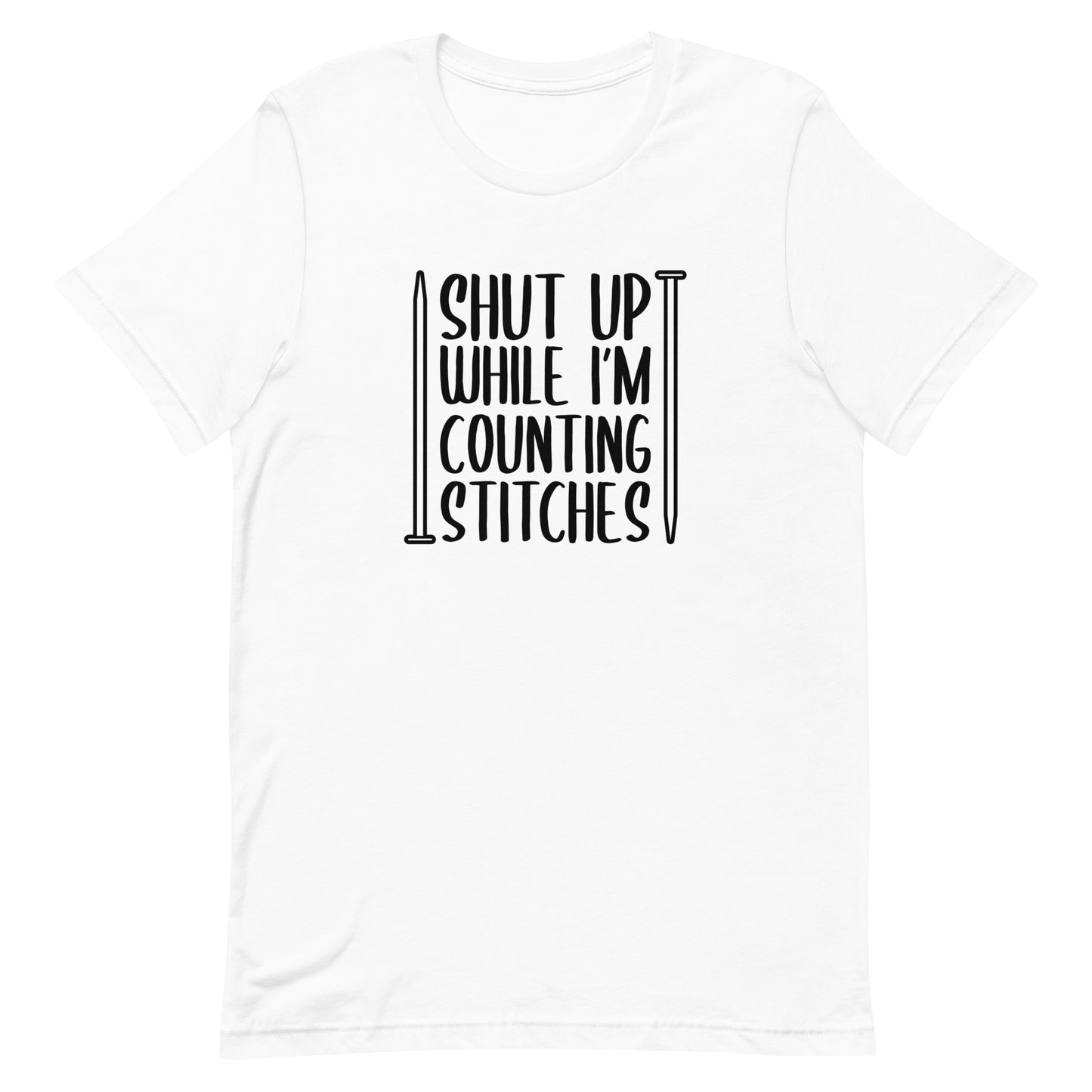A white crewneck t-shirt with black text surrounded by two knitting needles. The text reads "Shut up while I'm counting stiches".