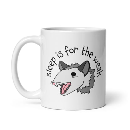 A white 11 ounce ceramic coffee mug featuring an illustration of an opossum with its mouth open, as if it was yelling. Text alongside the opossum reads "sleep is for the weak"