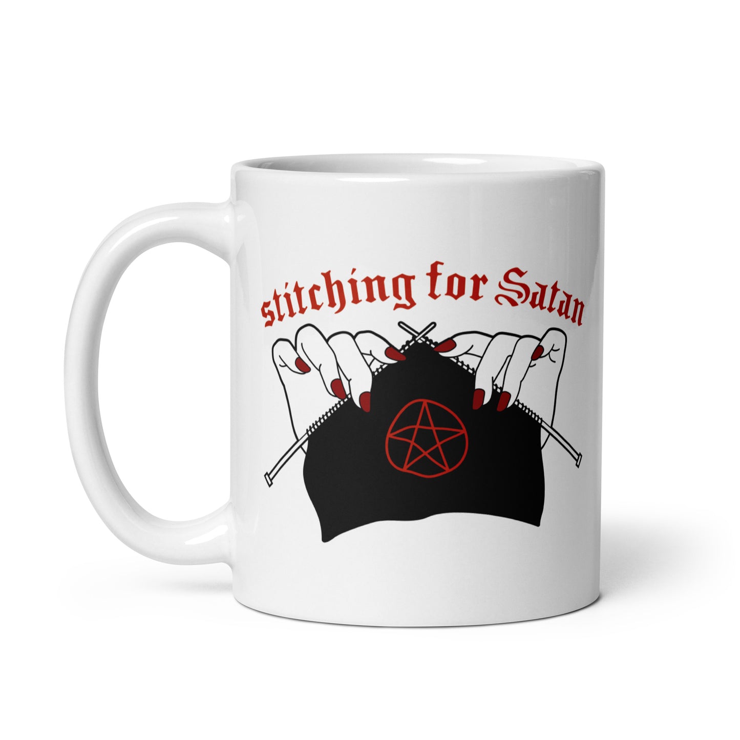 A white 11oz ceramic coffee mug featuring an illustration of pale white hands with red fingernails holding knitting needles. Fabric on the needles features a red pentagram. Text above the hands reads "stitching for Satan" in a gothc red font.