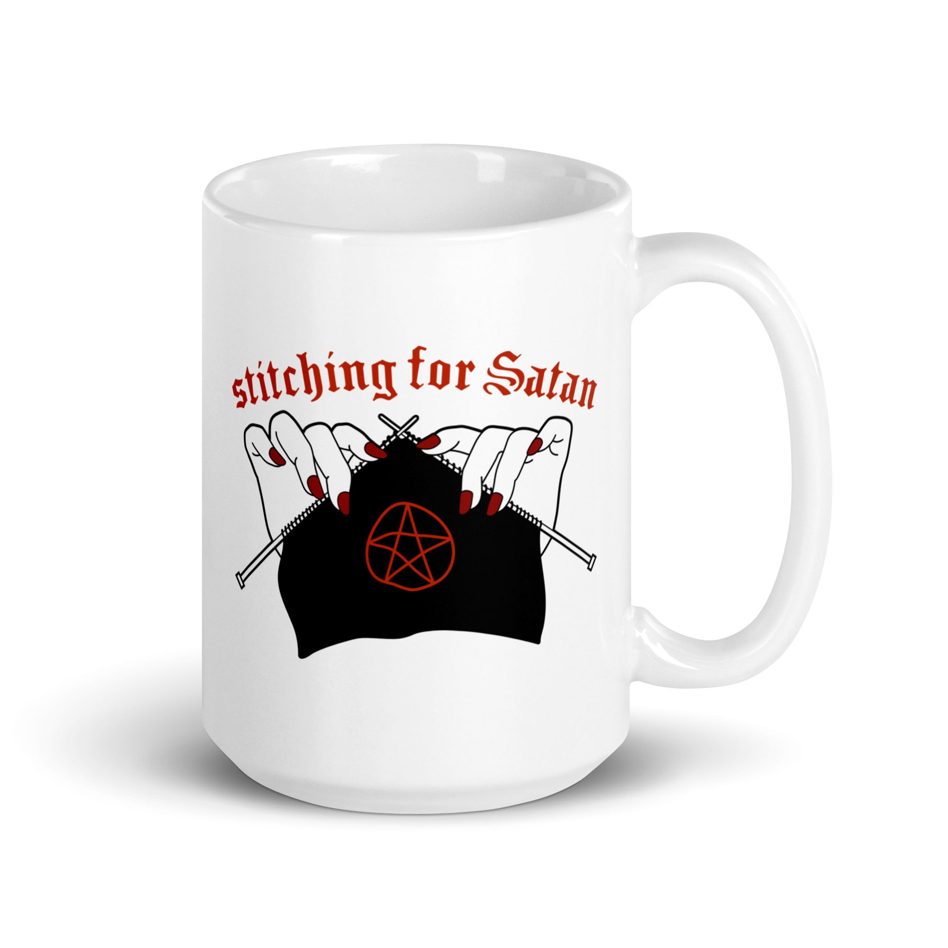 A white 15oz ceramic coffee mug featuring an illustration of pale white hands with red fingernails holding knitting needles. Fabric on the needles features a red pentagram. Text above the hands reads "stitching for Satan" in a gothc red font.
