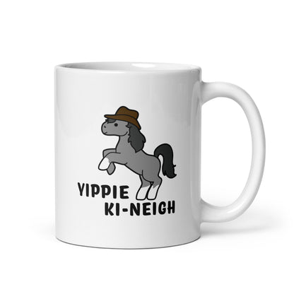 A white 11 ounce ceramic coffee mug featuring an illustration of a smiling grey pony rearing and wearing a cowboy hat. Text underneath the pony reads "Yippie Ki-Neigh"