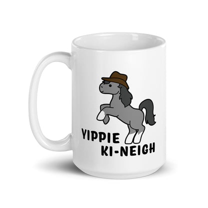 A white 15 ounce ceramic coffee mug featuring an illustration of a smiling grey pony rearing and wearing a cowboy hat. Text underneath the pony reads "Yippie Ki-Neigh"