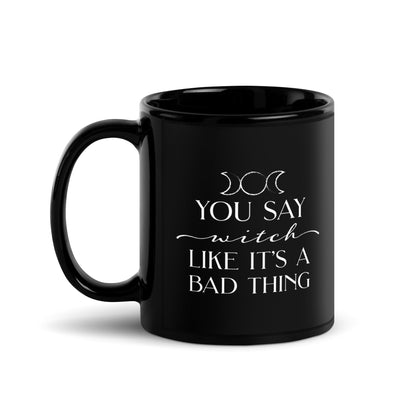 A black ceramic mug featuring the triple goddess symbol and text reading "You say witch like it's a bad thing"