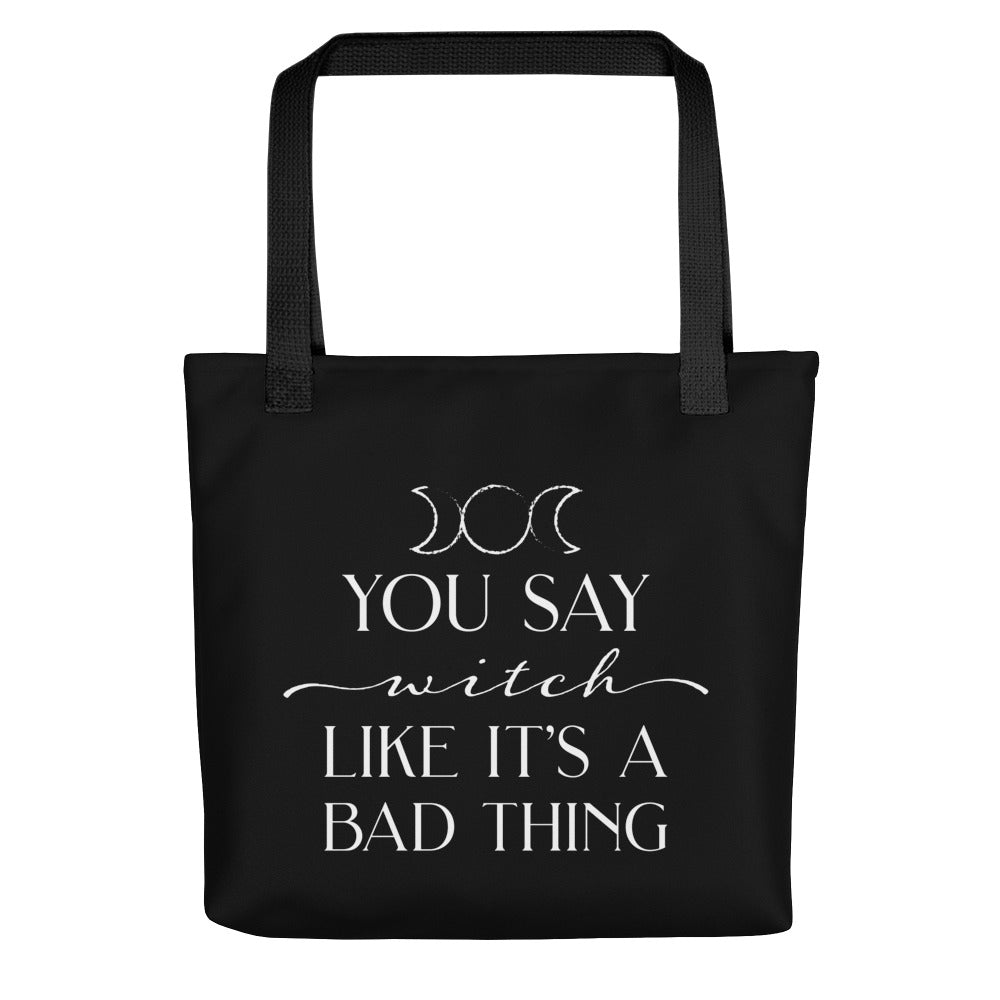 A black tote bag with black handles featuring the triple goddess symbol and text reading "You say witch like it's a bad thing"